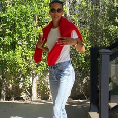 American fashion influencer Tylynn Nguyen poses in a white T-shirt, black wire-rim cat-eye sunglasses, red sweater over the shoulder, and straight-leg classic jeans