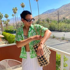 Woman on balcony in Palm Springs wearing a floral shirt, bikini, and white skirt with palm trees in the background