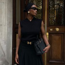 the best fall fashion finds under 150 are shown in a photo of a woman outside wearing a black sweater vest with a black belt and black skirt and black handbag