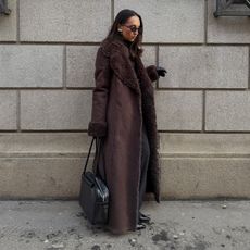 Ingrid wears a brown fur coat, black bag, black pants, and black leather gloves.